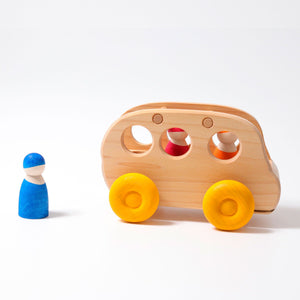 A wooden natural bus with yellow wheels. Side view with two peg people inside and one peg person outside.