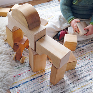 child playing with building blocks; built as a bridge with a wooden horse going through one arch