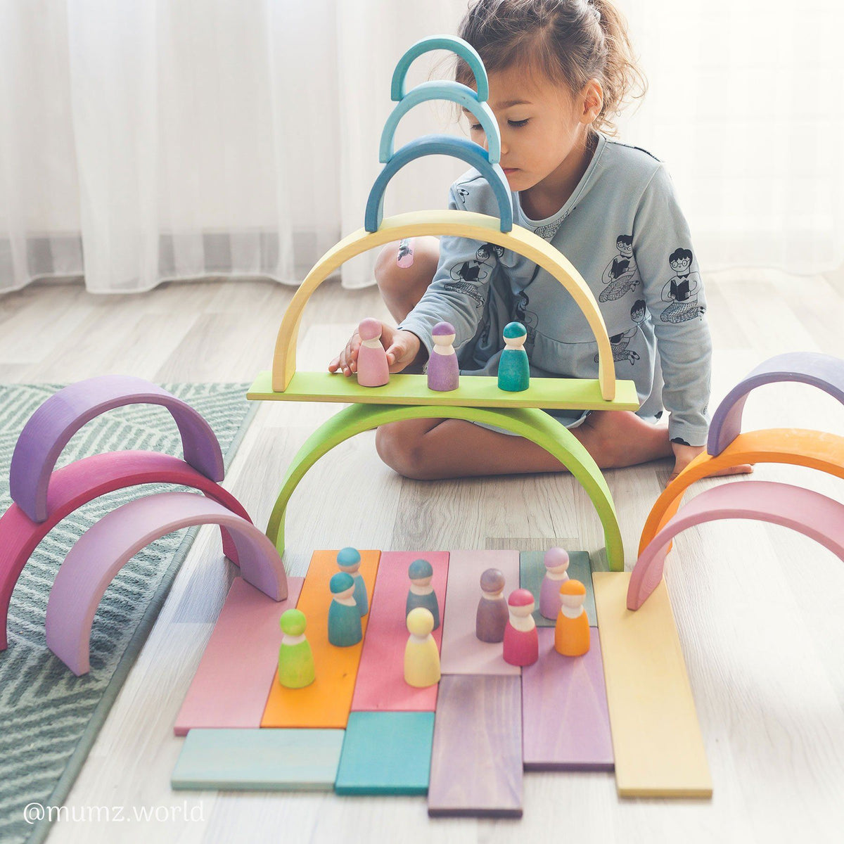 girl sitting on the floor building with pastel building boards, large pastel rainbow, and pastel friends