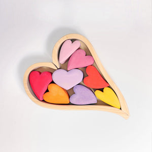 the red hearts set includes 8 different different colors in tints of reds, purples, and yellows. The hearts sit on a heart-shaped wooden frame enclosed by two natural wooden pieces that form a heart.