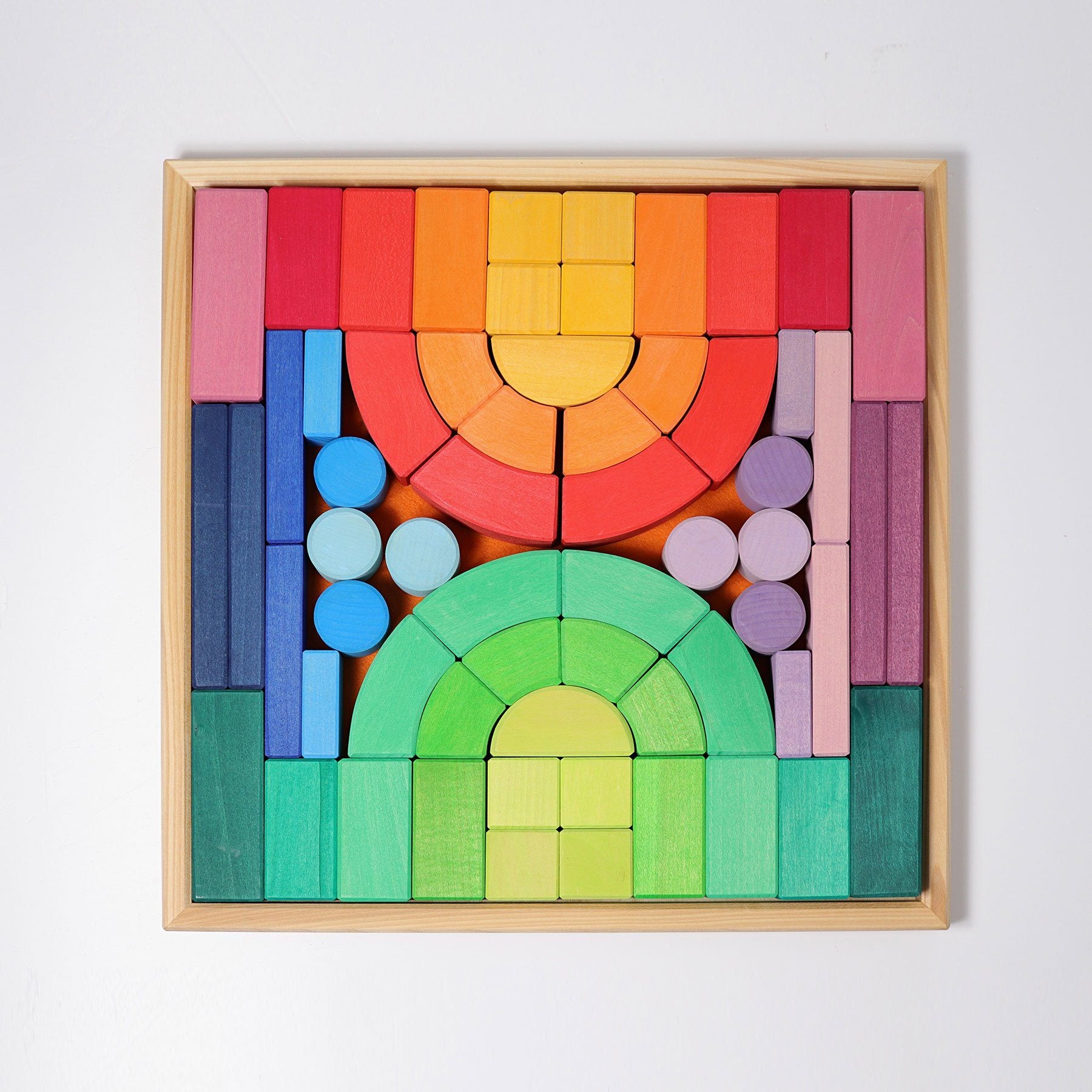 Romanesque building set in frame. Set includes 62 wooden building blocks in rainbow and pastel colors. Shapes range from pillars, rectangular blocks, square blocks, slates, and curved blocks.