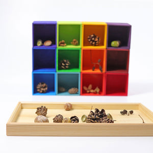 Rainbow boxes are out and stacked behind the frame. There are natural elements in the frame such as pine cones, acorns, and leaves. These elements are also picture resting in the rainbow boxes in the back.