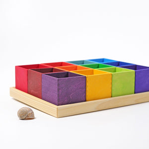 12 rainbow boxes in a natural wood frame. The colors of the boxes match the Grimm's rainbow sets. Side view next to a shell to show size.